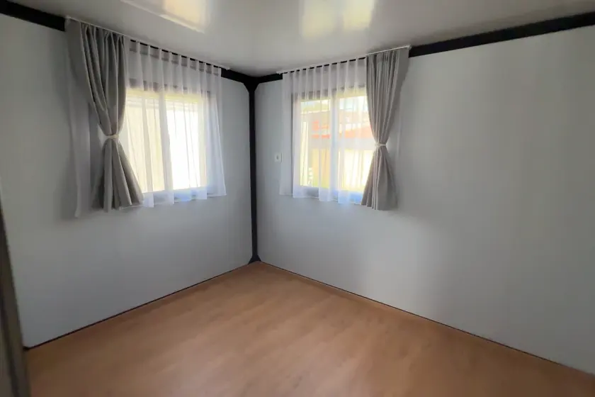 Prázdný interiér domu se dvěma okny a dřevěnou podlahou
